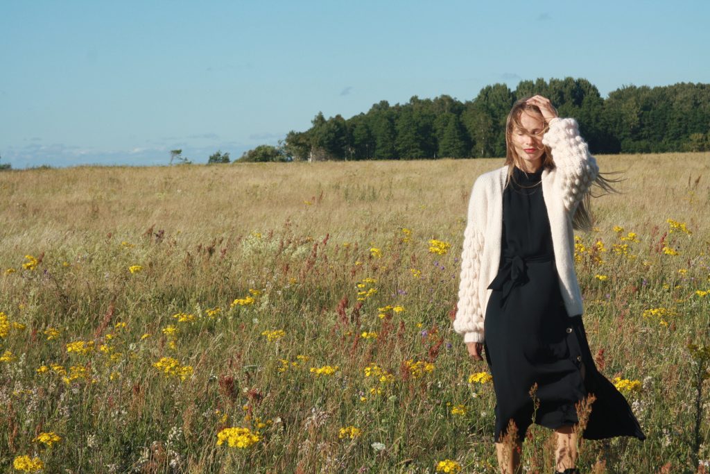 Meitene ar melnu kleitu un baltu adītu jauku pļavā